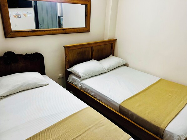 A bedroom with two single beds, a wooden headboard, a mirror, and a wall socket. - Hotel El Progreso (Armenia)