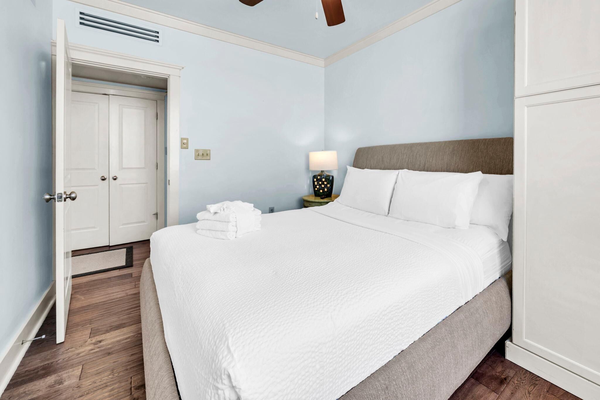 A neatly made bed with white linens, a bedside lamp, and a door to a closet.