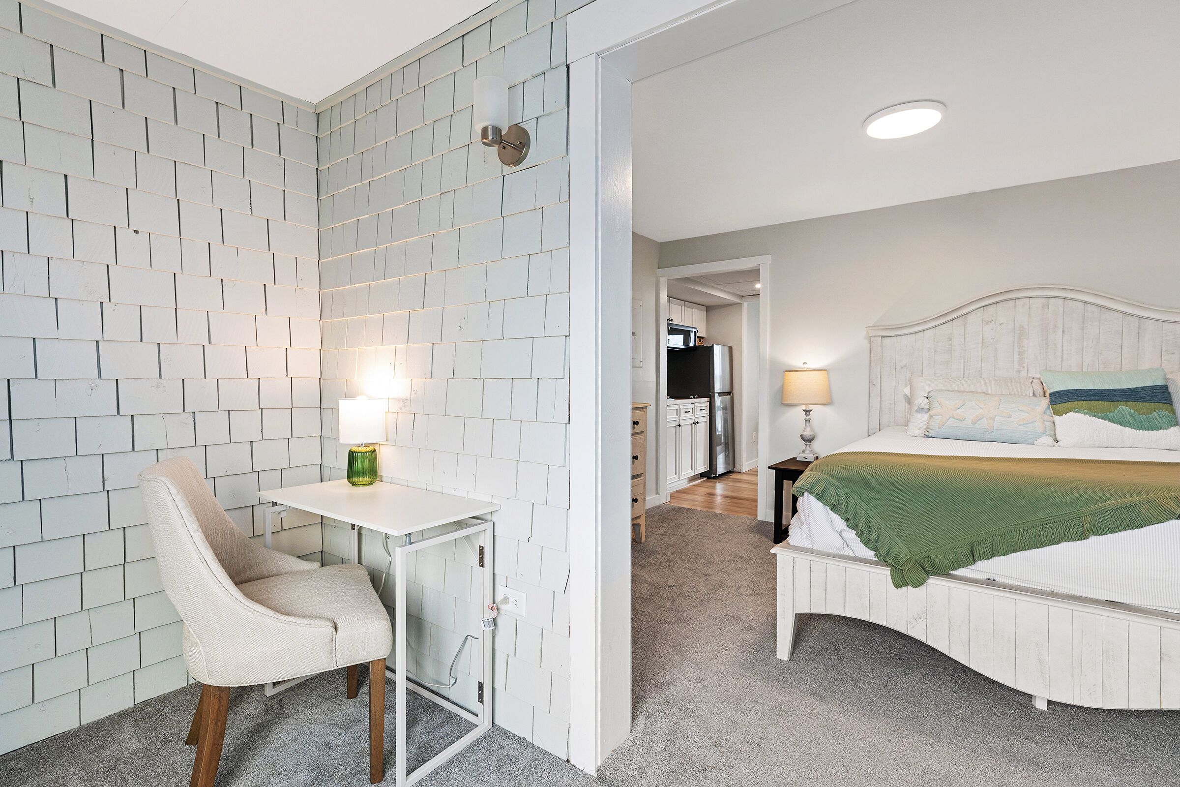 A bedroom with a bed, a chair, a desk, and a wall with a brick pattern.
