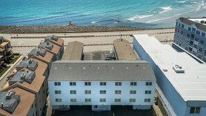 A coastal building with multiple floors, a parking lot, and a view of the ocean and beach. - Twin View: 1 BR, Living Room, Ocean & Marsh Views, Beach Chairs, 1 parking spot (Hampton)
