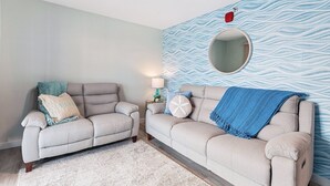 A living room with two sofas, a rug, a lamp, and a wall with a wavy pattern. - Twin View: 1 BR, Living Room, Ocean & Marsh Views, Beach Chairs, 1 parking spot (Hampton)
