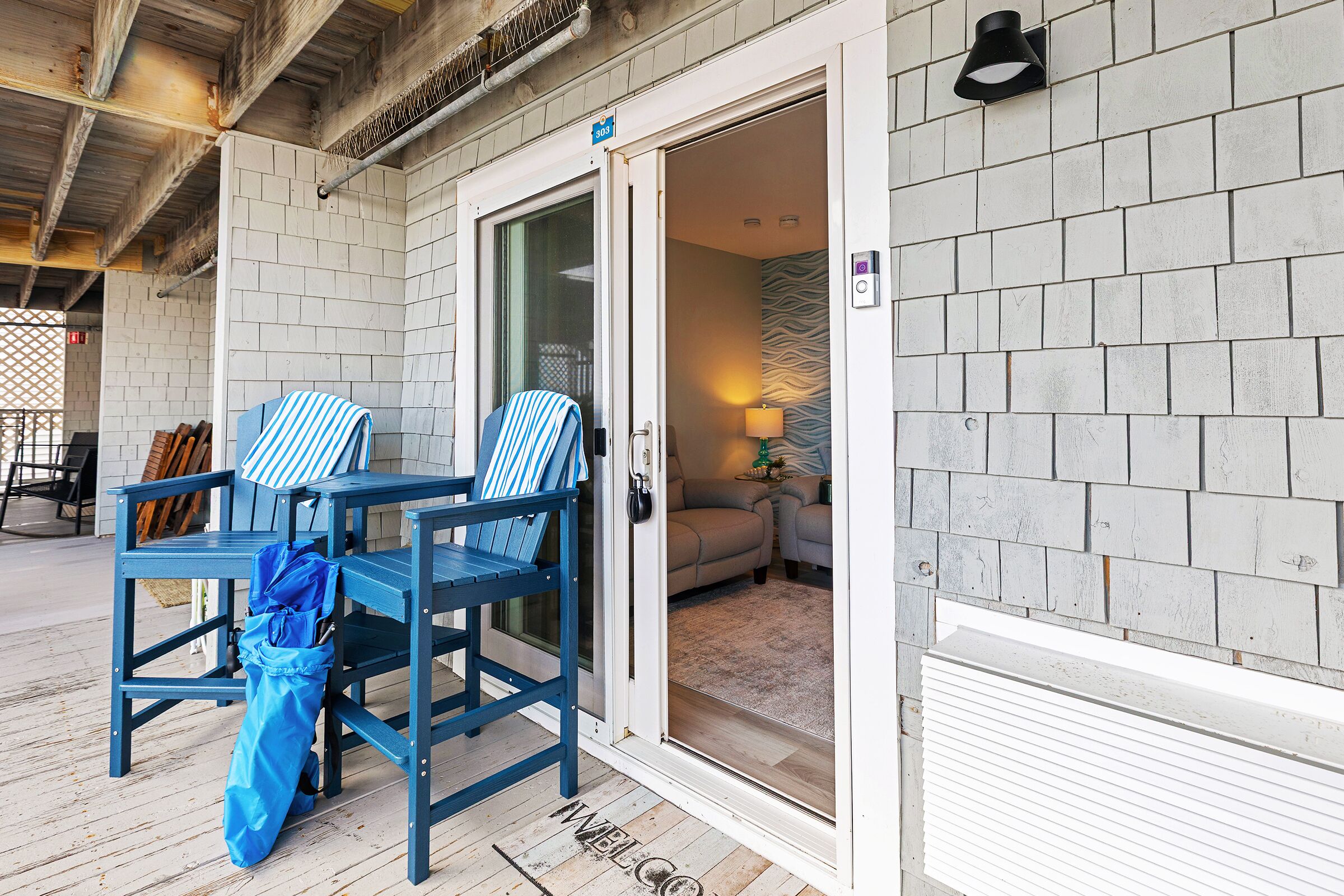 A hotel entrance with a door, a blue chair, a blue umbrella, and a welcome mat.