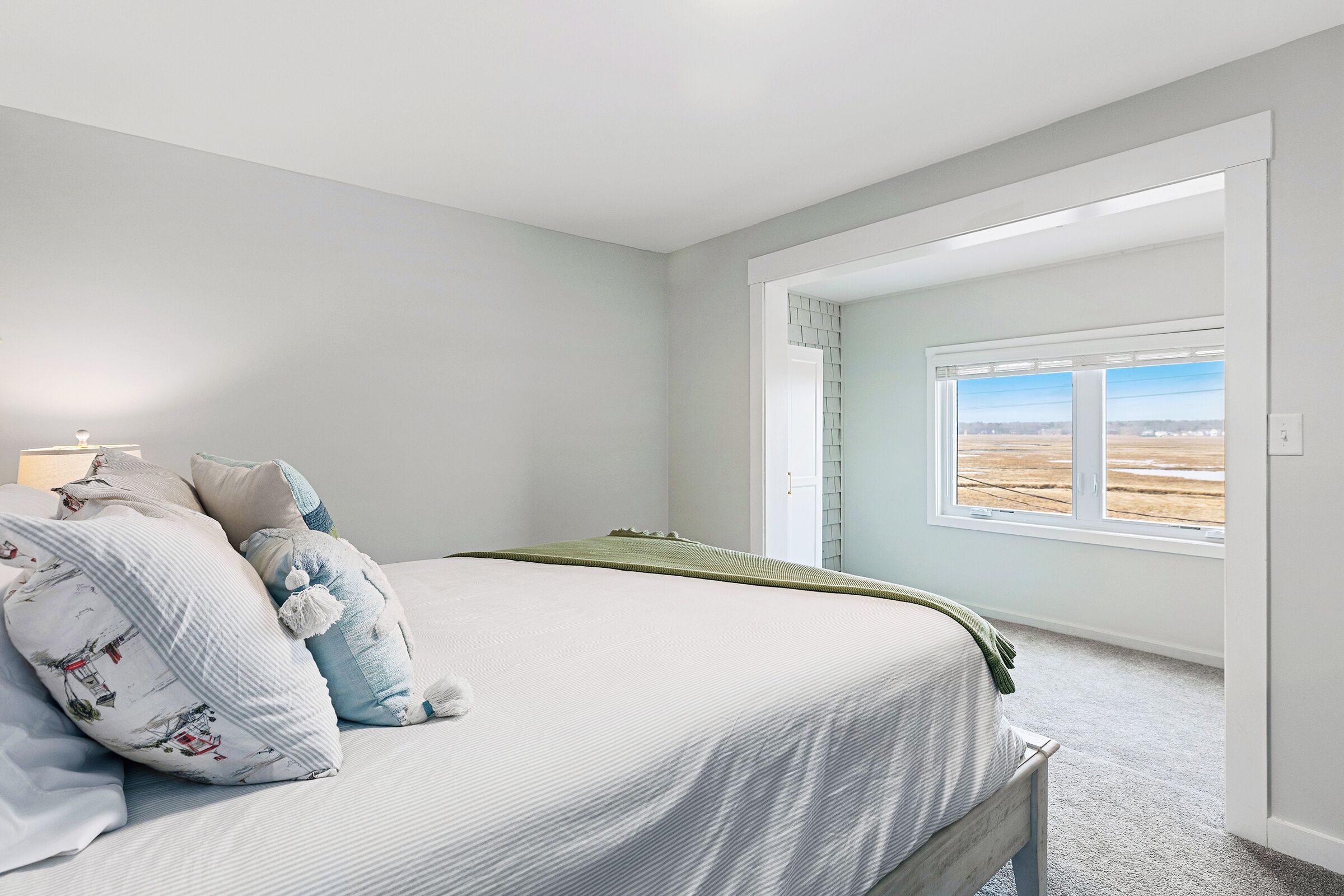 A bedroom with a large bed, a window with a view, and a door leading to another room.