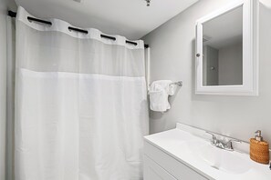 A bathroom with a shower curtain, a sink, a mirror, and a towel rack. - Twin View: 1 BR, Living Room, Ocean & Marsh Views, Beach Chairs, 1 parking spot (Hampton)