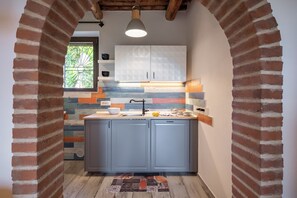 A kitchen with a brick archway, a window with a decorative grille, and a modern light fixture. - Countryside with sea view (Follonica)