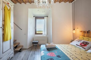 A bedroom with a bed, a window with curtains, a radiator, a small stool, and a chandelier. - Countryside with sea view (Follonica)