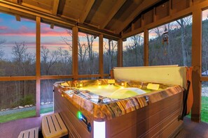 Ein Whirlpool mit Holzverkleidung, einer Sitzbank und Blick auf Bäume durch große Fenster.