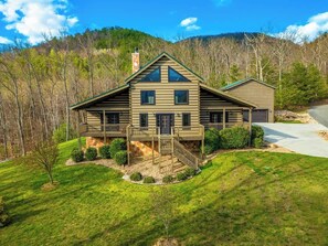 A two-story log cabin with a front deck, a stone chimney, and a driveway leading to a garage. - Luxury, Chalet with Private Suite, Secluded, and HotTub (Cosby)