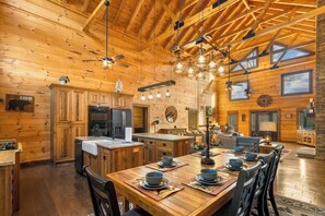 A spacious log cabin interior with a large dining table, wooden cabinets, and a kitchen area. - Luxury, Chalet with Private Suite, Secluded, and HotTub (Cosby)