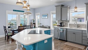 A kitchen with a central island, grey cabinets, and pendant lighting. - Fall Beach & Golf Getaway! Ocean View, Heated Pool, Elevator, Steps to Beach (Ocean Isle Beach)