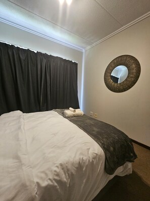Ein Hotelzimmer mit einem Bett, einem dunklen Vorhang, einem Wandspiegel und einem Lichtschalter.