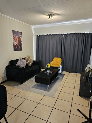 A living room with a black sofa, a yellow armchair, and a black coffee table. - Cozy One-Bedroom Apartment In Fourways (Sandton)