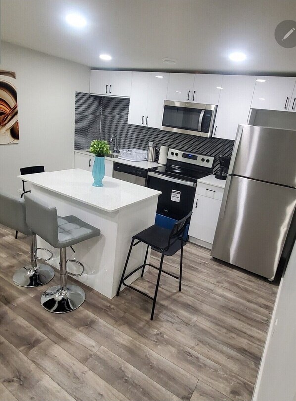 Una cocina moderna con armarios blancos, electrodomésticos de acero inoxidable, una isla central con taburetes y un salpicadero blanco y negro.