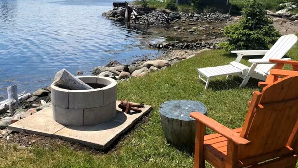 Un área al aire libre junto al lago con sillas Adirondack, una hoguera y un cobertizo pequeño.