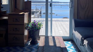 Una habitación con detalles de madera, un ventanal corredizo hacia un muelle, un tapete azul y blanco, un aparador de madera y una planta en maceta.