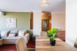 Un salon avec un canapé, une table à manger agrémentée d’une plante en pot et un couloir menant à une salle de bain.