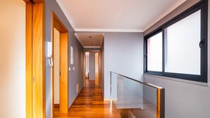 A modern hallway with wooden flooring, a glass railing, and a view through a window.