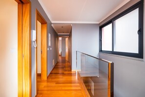 A modern hallway with wooden flooring, a glass railing, and a view through a window. - GuestReady - Tyler house in Funchal (Funchal)