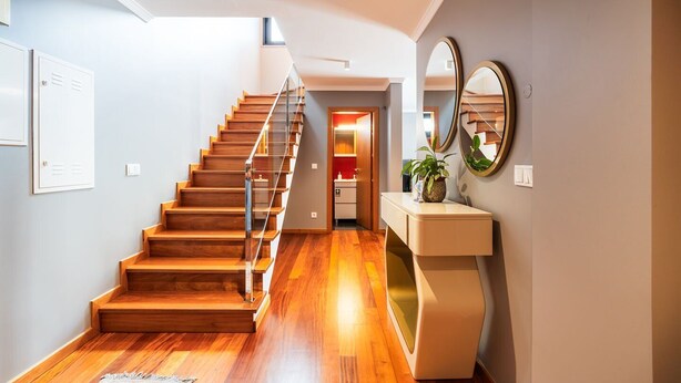 A modern interior with a wooden staircase, a white console table, and two wall mirrors.