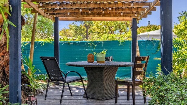 A wooden deck with a round table and two chairs, surrounded by greenery and a green fence. - Garden Oasis Room near Wynwood (Miami)