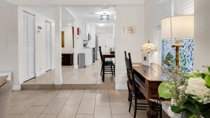 A modern kitchen with white cabinets, a dining area with a wooden table and chairs, and a hallway leading to a bedroom. - Garden Oasis Room near Wynwood (Miami)
