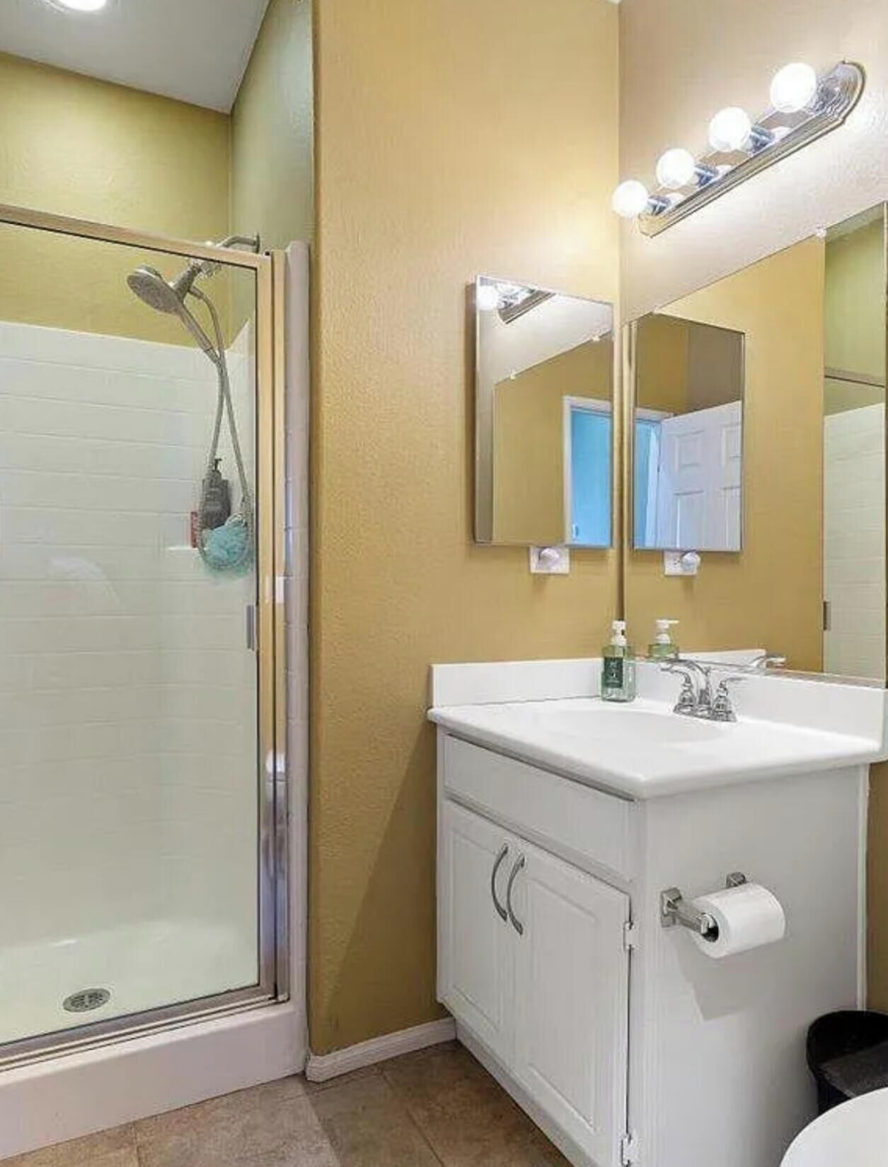 Ein Badezimmer mit Duschkabine aus Glas, einem weißen Waschbecken mit Spiegel darüber und einer Toilette.