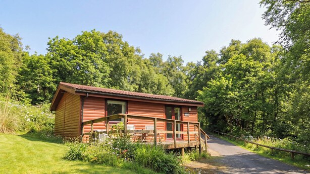 Eine Holzhütte mit Veranda, umgeben von üppigem Grün und einem Kiesweg.