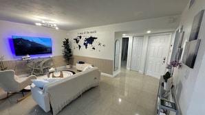 A modern living room with a flat-screen TV, a white sofa, a coffee table, and a world map on the wall. - 3bedroom-Free Parking LakeView-Sunset-Balcony-Central - 24hr Security Patrol (Homestead)