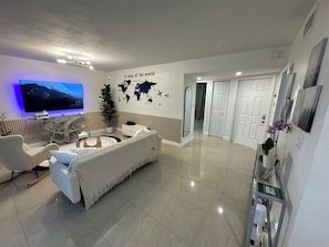 A modern living room with a flat-screen TV, a white sofa, a coffee table, and a world map on the wall.