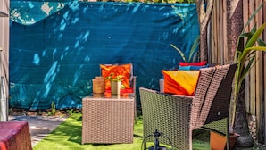 A patio area with wicker furniture, a small table with a vase, and a blue tarp in the background. - Private Room Near Wynwood Free Parking (Miami)