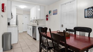 A compact kitchen with white cabinets, a dining table with chairs, and a small trash bin. - Private Room Near Wynwood Free Parking (Miami)