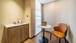 A modern hotel room with a wooden cabinet, a small round table with a laptop, and a single orange chair. - Wuzhou Hotel (Pinghu)