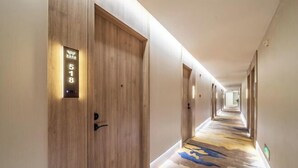 A hotel hallway with wooden doors, a carpeted floor, and a long corridor. - Wuzhou Hotel (Pinghu)