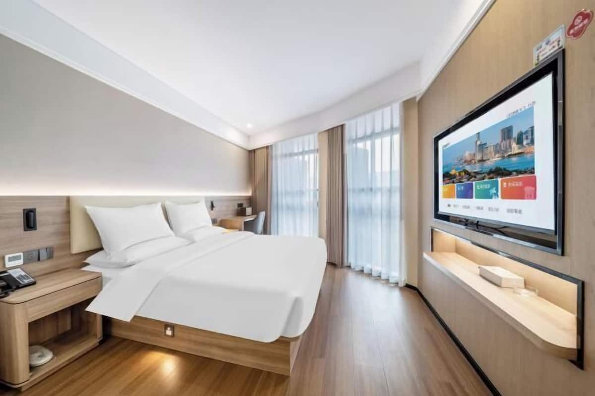 Habitación de hotel moderna con una cama grande, un televisor montado en la pared y piso de madera.
