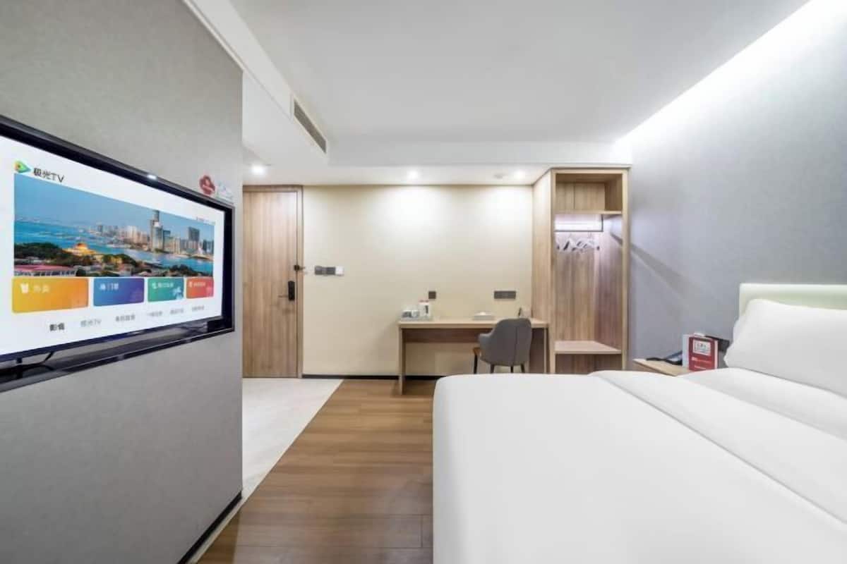 Habitación de hotel con cama, escritorio, silla, televisor montado en la pared y armario de madera.