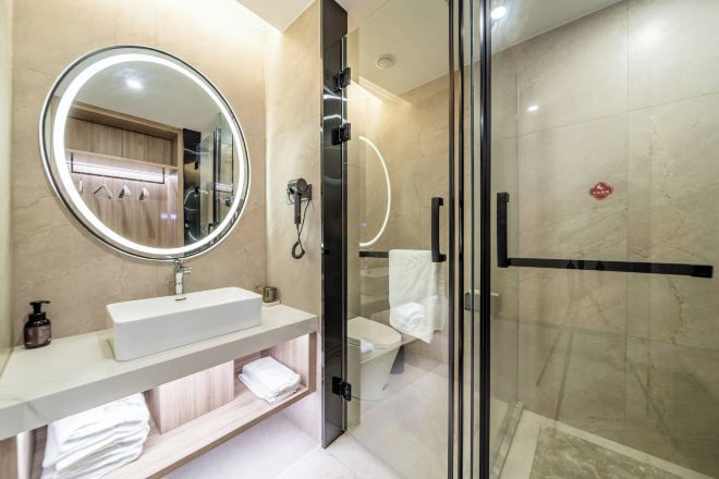 Un baño moderno con un espejo redondo, un lavabo blanco, una cabina de ducha con mampara de cristal y un perchero para toallas.