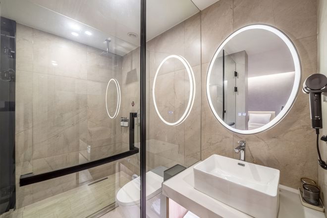 Un baño moderno con cabina de ducha de vidrio, un lavabo blanco y dos espejos redondos con marcos iluminados.