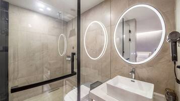 Un baño moderno con cabina de ducha de vidrio, un lavabo blanco y dos espejos redondos con marcos iluminados.