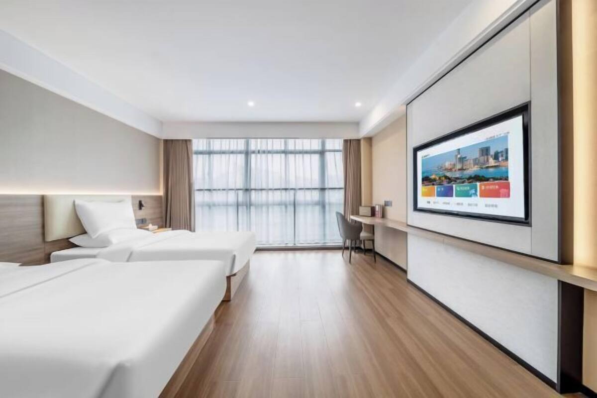 A hotel room with two beds, a desk, a TV, and a large window.