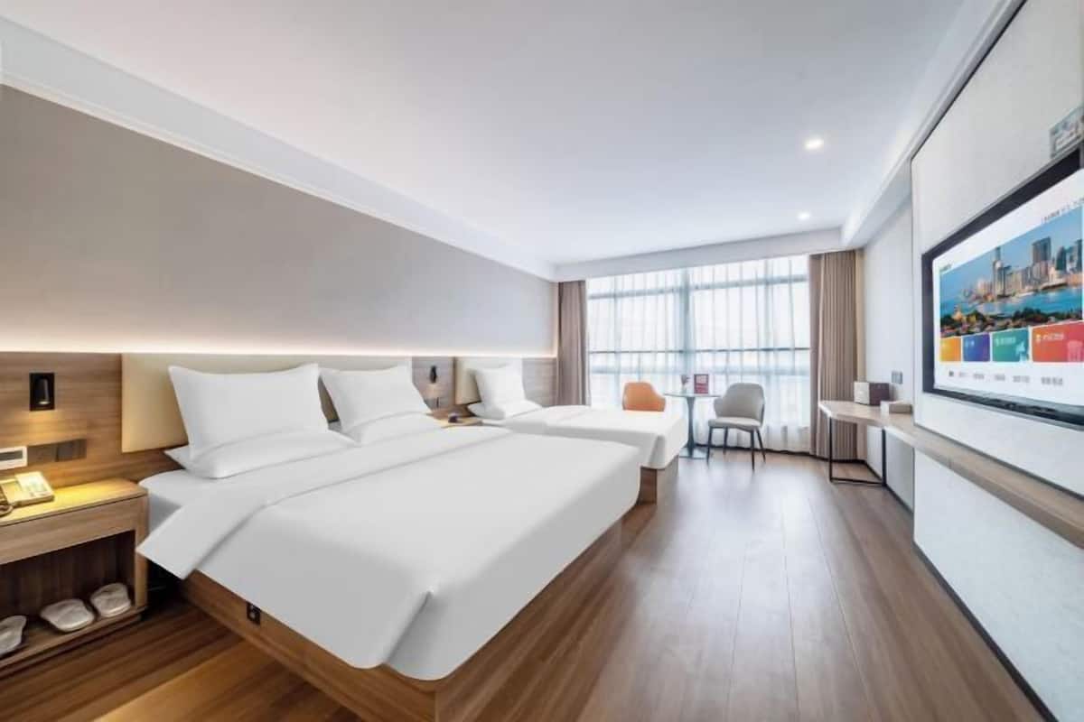 Una habitación de hotel con dos camas, un escritorio, una silla y un ventanal grande.