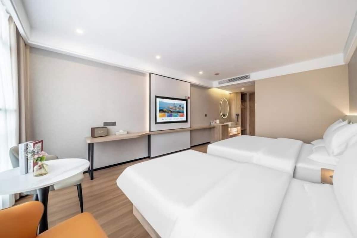 Habitación de hotel con una cama grande, una mesita, una silla, un escritorio, un espejo y un cuadro en la pared.