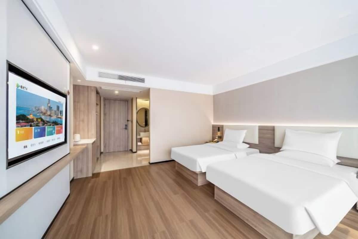 Habitación de hotel con dos camas, un televisor montado en la pared y piso de madera.