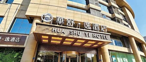 A hotel entrance with a sign indicating 'HUA SHU YI HOTEL' and a revolving door.