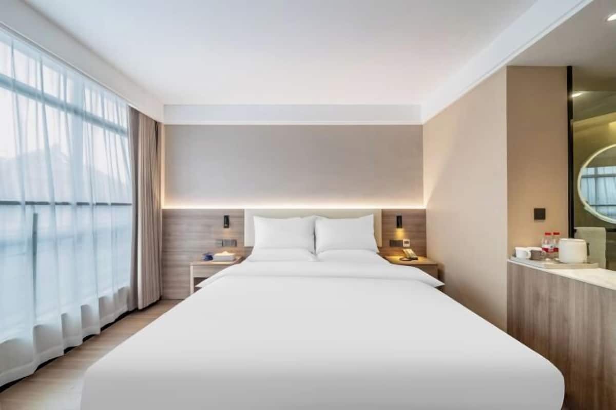 Una habitación de hotel moderna con una cama grande, mesitas de noche, un espejo y una ventana con cortinas.