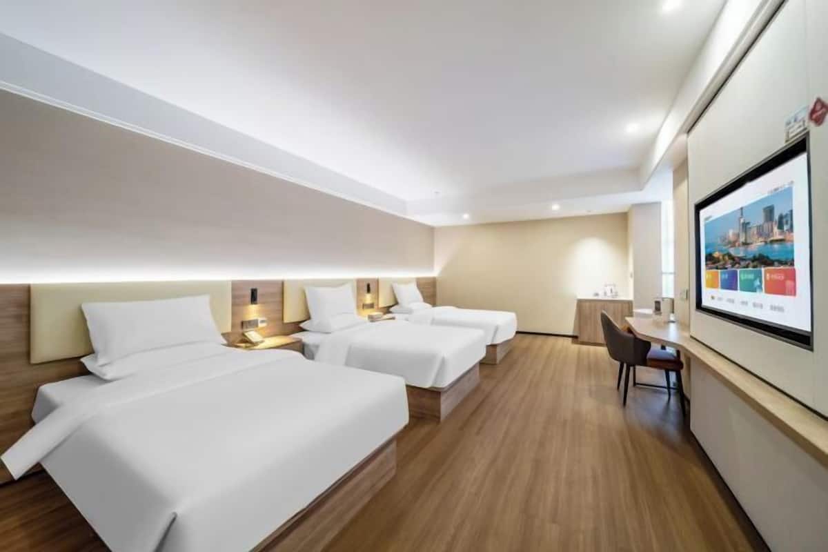 Habitación de hotel con dos camas, un escritorio y un televisor en la pared.