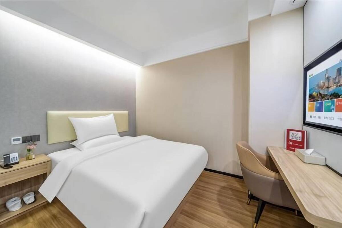 Una habitación de hotel con cama, escritorio, silla, televisor y zapatero.