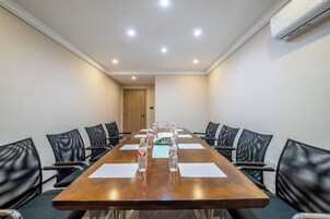 Un salón de conferencias con una larga mesa, sillas negras y botellas de agua sobre la mesa.