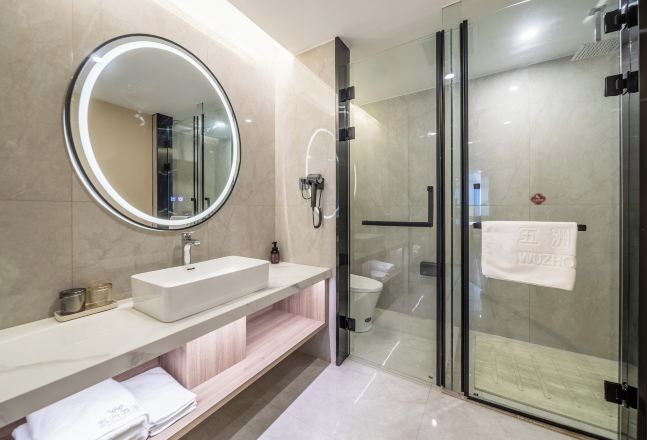 Un baño moderno con un espejo redondo, un lavabo blanco, una cabina de ducha de vidrio y un perchero para toallas.