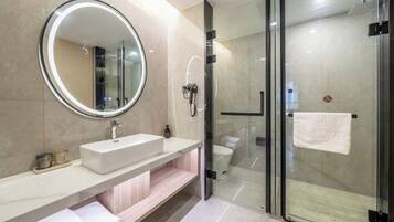 Un baño moderno con un espejo redondo, un lavabo blanco, una cabina de ducha de vidrio y un perchero para toallas.