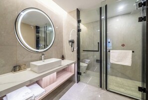 Un baño moderno con un espejo redondo, un lavabo blanco, una cabina de ducha de vidrio y un perchero para toallas.